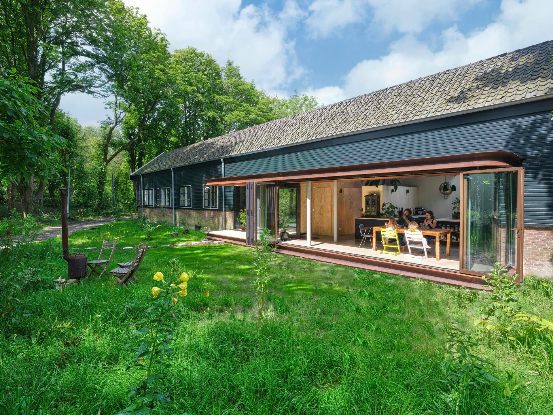 Lang gebouw met donkere gevel en open schuifpui, gezien vanuit de tuin